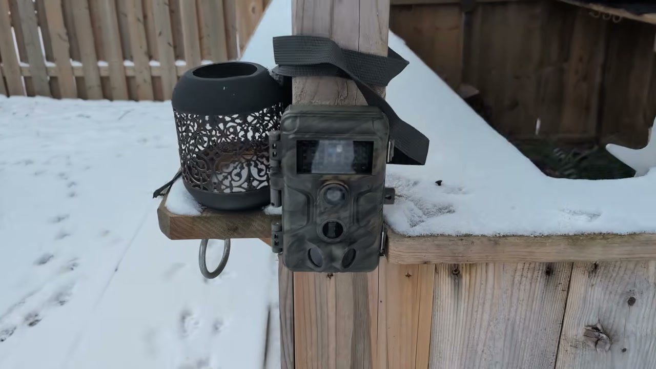 A GardePro A3S trail camera strapped to a snowy deck post