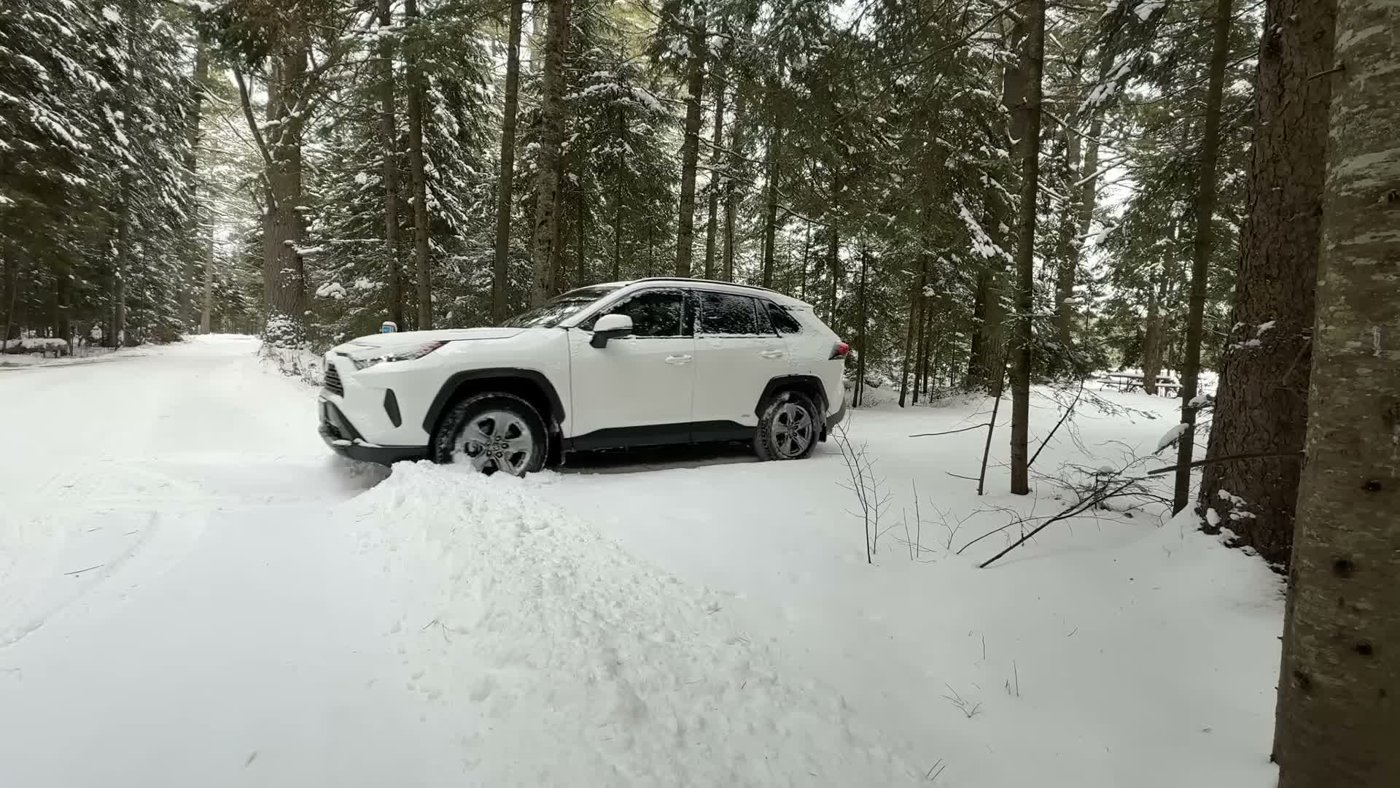 A white RAV4 Hybrid parked at a snowy campsite in a pine forest