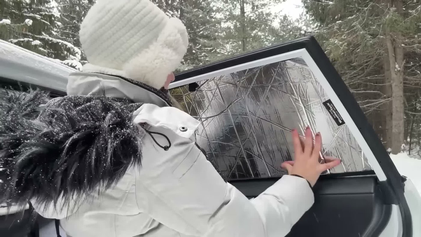 A reflective window cover being fitted into a RAV4 rear door window in the snow
