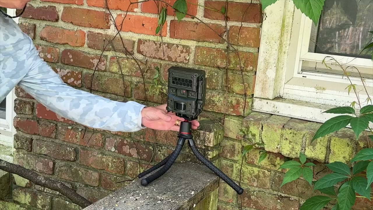 An owner setting up a Reconyx HyperFire 4K trail camera on a small tripod outside his house