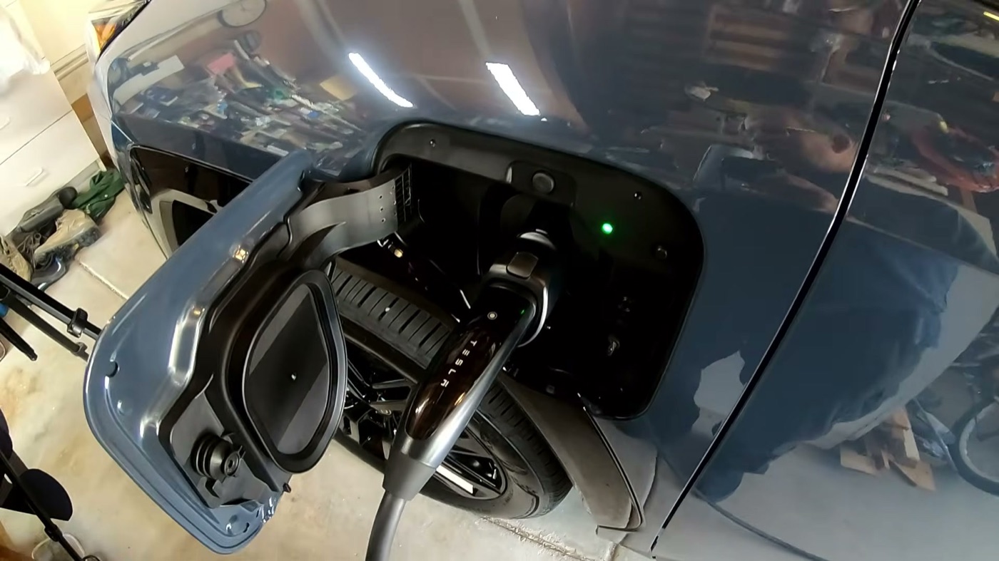 A blue 2026 RAV4 Plug-in Hybrid XSE in a home garage with its charge port door open and a Tesla wall charger's plug connected
