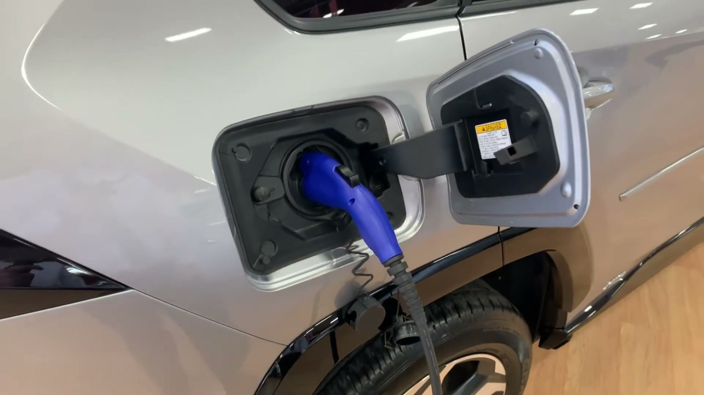 A silver 2021 RAV4 Prime with its charge port door open on the rear passenger side and Toyota's blue charging cable plugged in