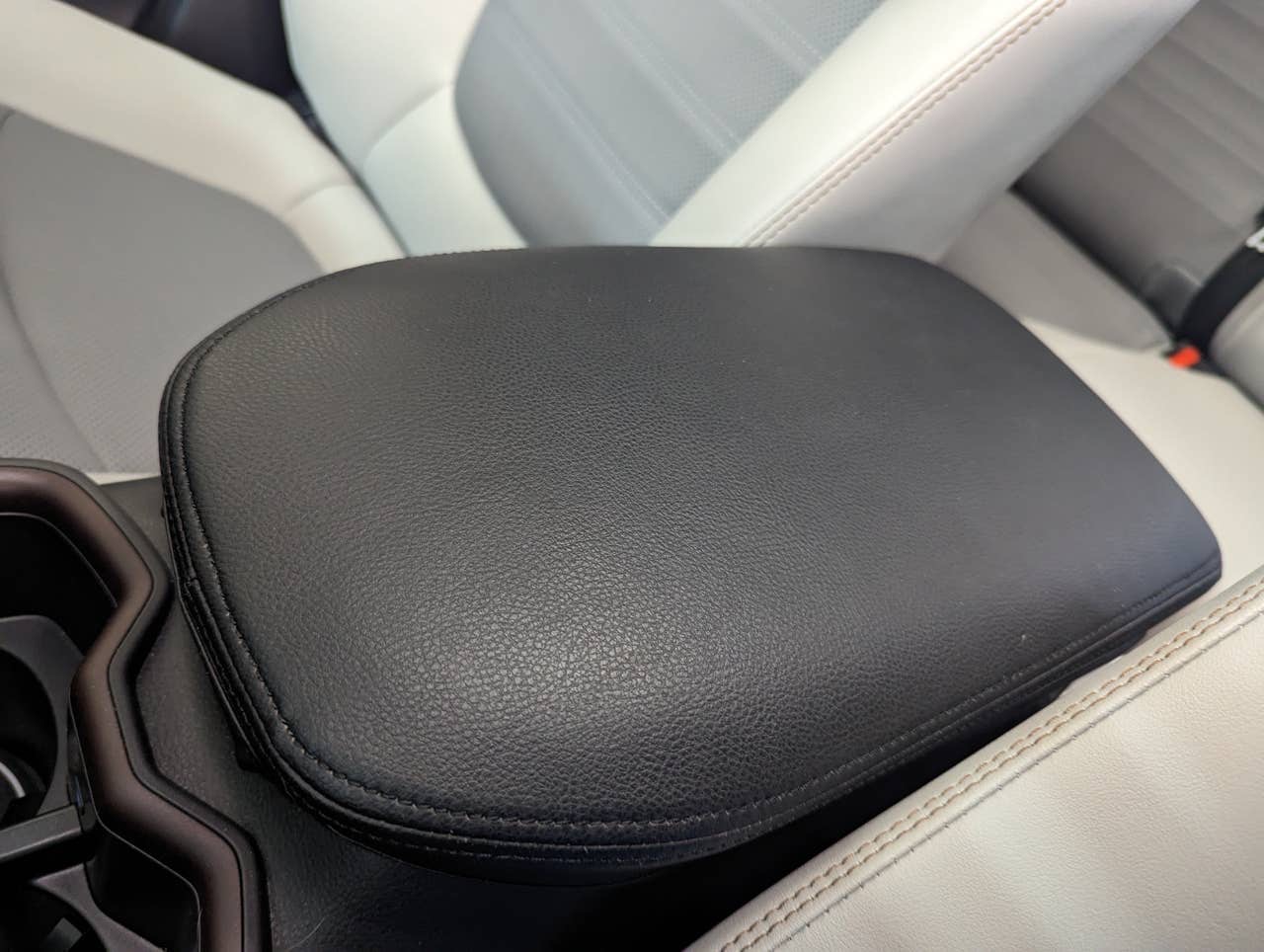 A black INTGET cover on the armrest of a 2023 RAV4 Limited with light gray seats