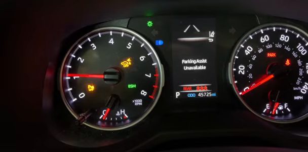 The gauges of a 2019 RAV4 after the 12-volt battery was disconnected, with the orange PKSB OFF light flashing in the tachometer and the gauge screen showing Parking Assist Unavailable