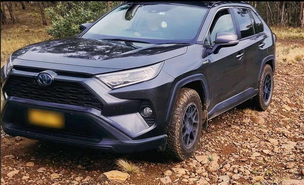 A dark gray RAV4 Hybrid on black KMC KM708 Bully wheels and Falken Wildpeak A/T3W tires on a rocky forest track