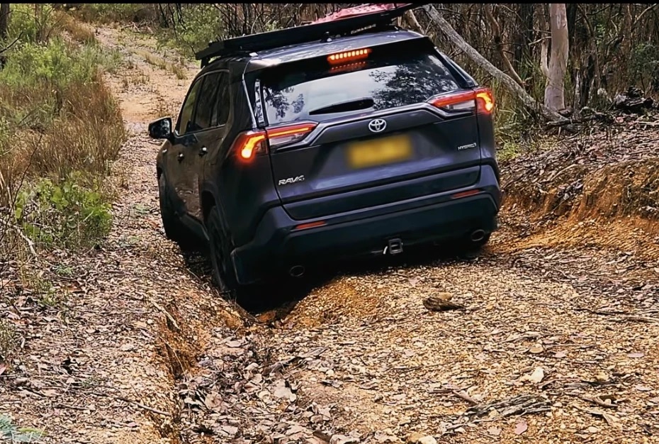 The RAV4 Hybrid climbing a rutted dirt track with a roof rack