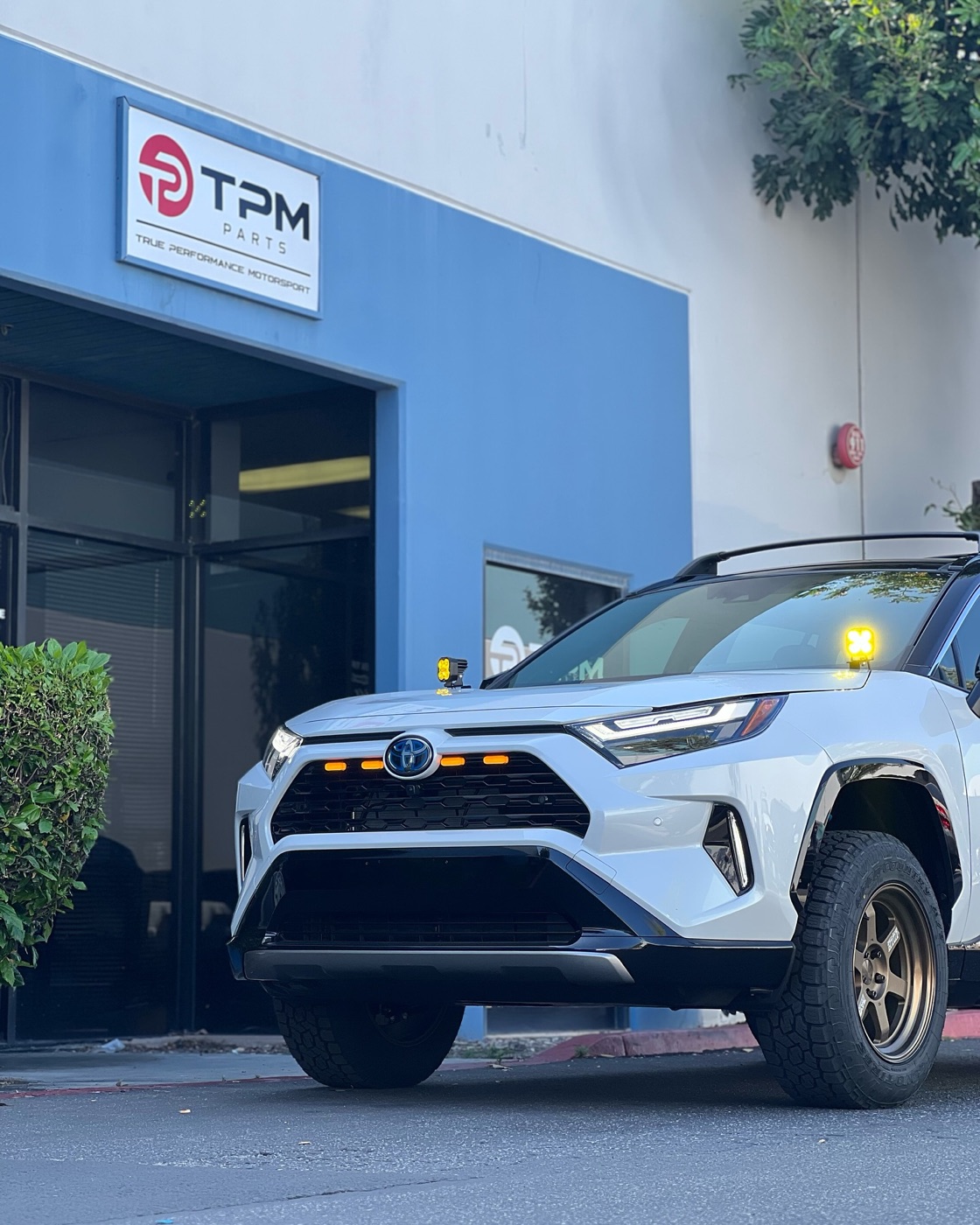 A white RAV4 Hybrid XSE with a black roof, a 2-inch lift, bronze Volk TE37 wheels, Toyo Open Country A/T III tires and amber grille and ditch lights