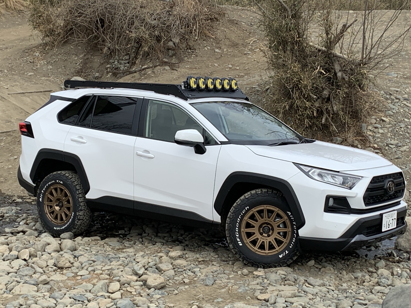 A white 2021 RAV4 on satin gold Icon Alloys Ricochet wheels and white-letter BFGoodrich KO2 tires, with a light bar on the roof rack