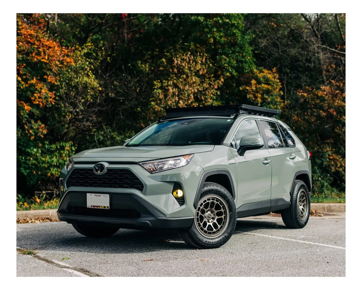 A Lunar Rock 2021 RAV4 XLE on bronze Reika R30 wheels and Yokohama Geolandar tires in 235/65R17, with a flat roof rack and yellow fog lights