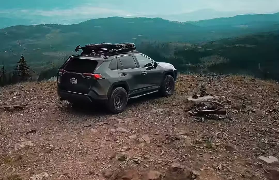 A lifted gray RAV4 TRD Off-Road with a roof rack, side steps and black 16-inch wheels parked on a mountain overlook