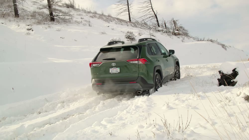 A green RAV4 TRD Off-Road on factory Falken Wildpeak A/T Trail tires climbing a snowy hill